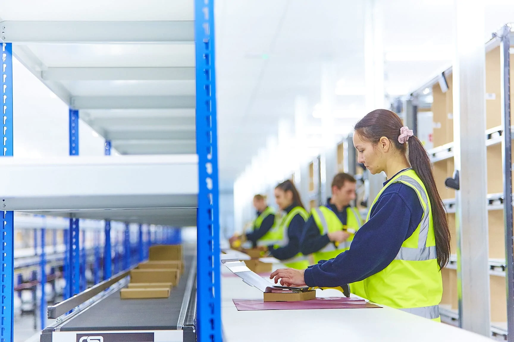 Four warehouse employees packaging up boxes for a conveyor belt