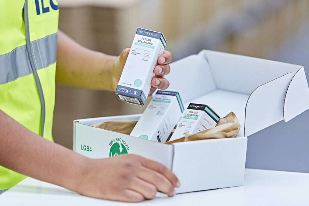 ILG warehouse employee in a high vis jacket packing a box of beauty products